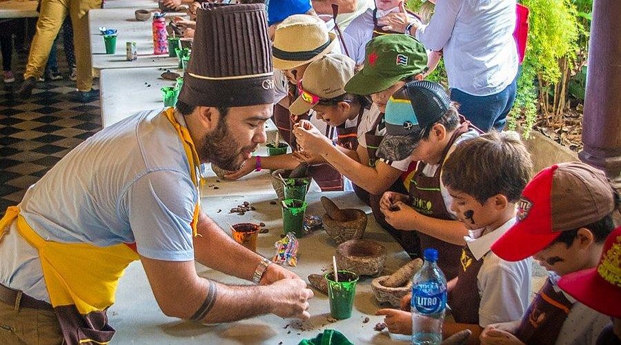 Besucher in braunen Schürzen mahlen Kakaobohnen von Hand in der Schokoladenwerkstatt „Bate Bate“ in Granada, Nicaragua