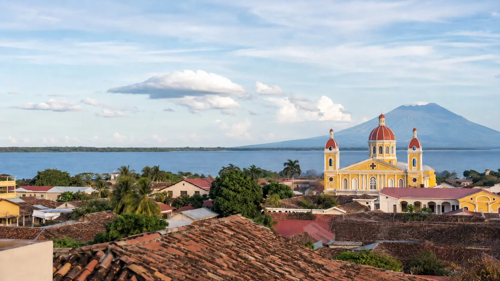 Morning view of Granada, Nicaragua with colonial rooftops, Lake Nicaragua, the yellow cathedral, and Mombacho Volcano in the background.