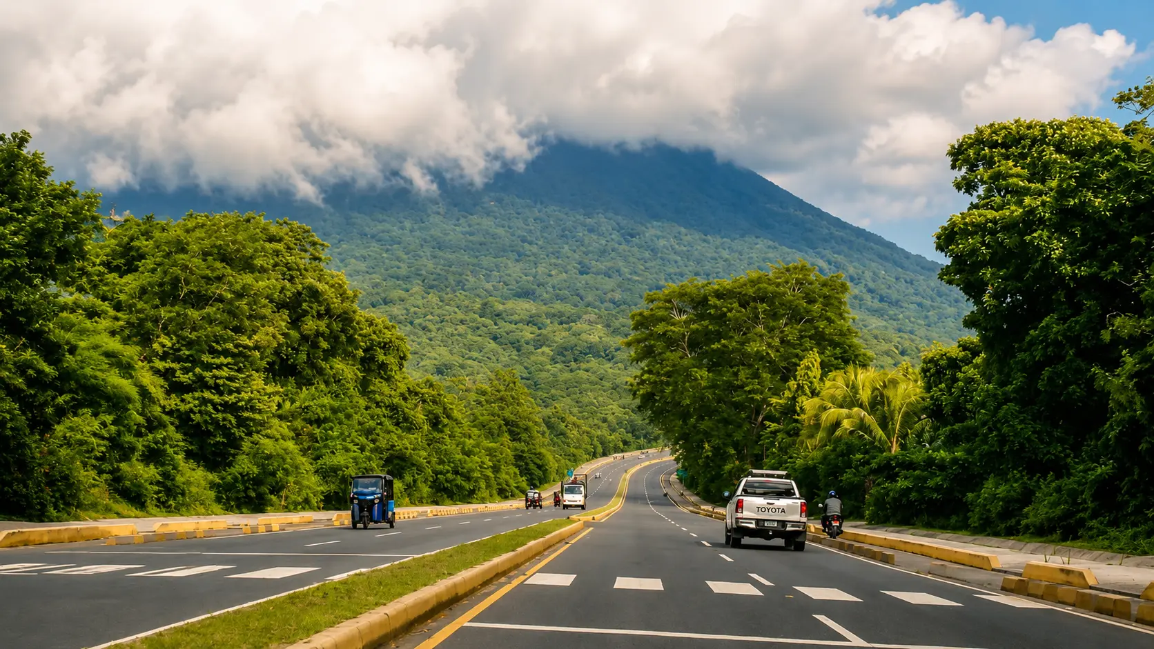 Road through lush green forest in Nicaragua with vehicles driving toward Volcán Mombacho under low clouds. The cloudy mountain backdrop shows why weather matters when planning the best time for a Nicaragua day trip from Guanacaste.