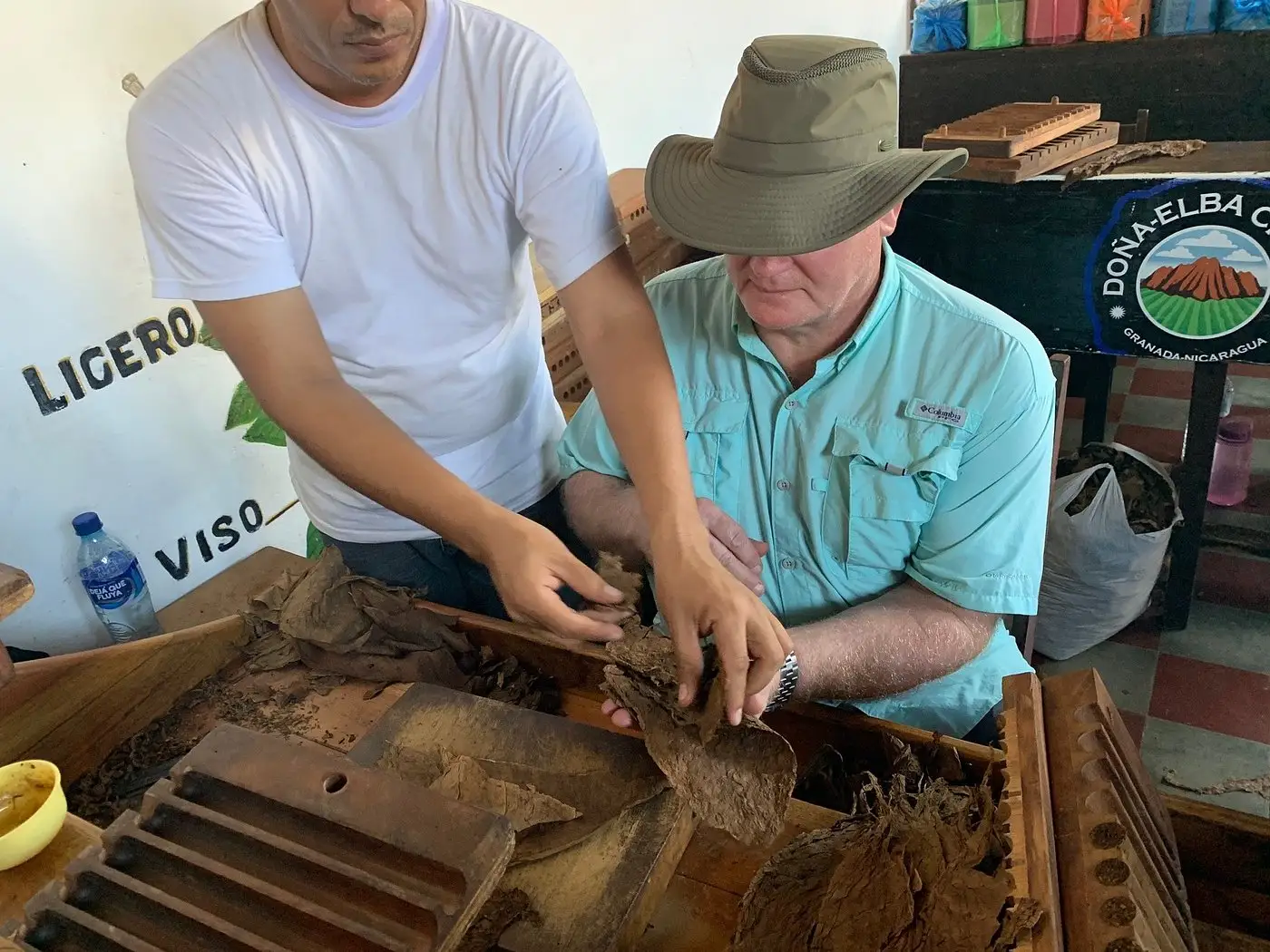 A tourist in a sun hat learning how to roll premium tobacco leaves from a local expert at Doña Elba Cigars factory in Granada, Nicaragua.